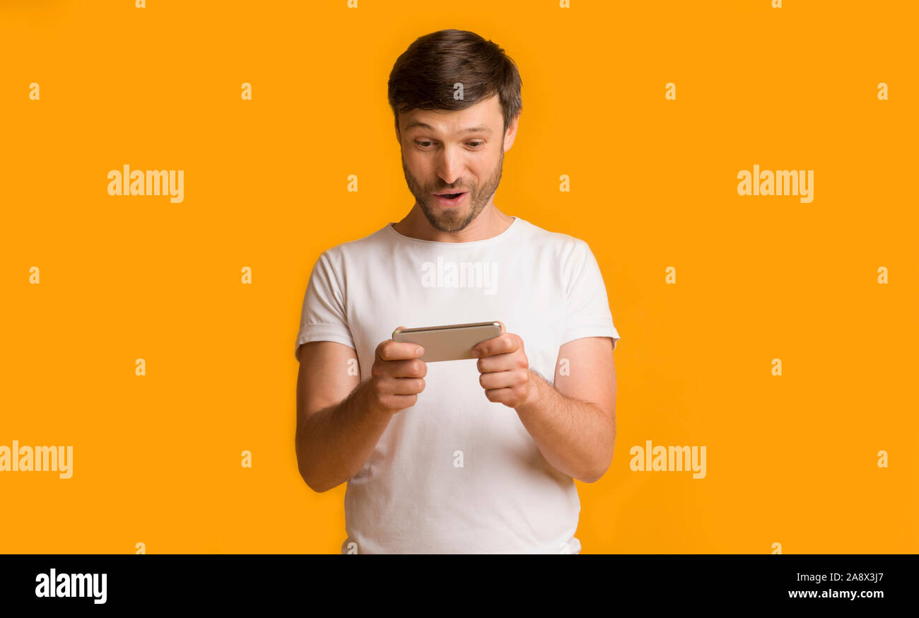 Man Playing On Smartphone Standing Over Yellow Studio Background Stock Photo