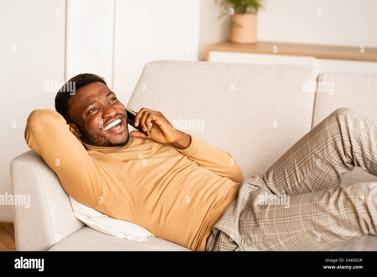 Afro Man Talking On Cellphone Lying On Couch At Home Stock Photo