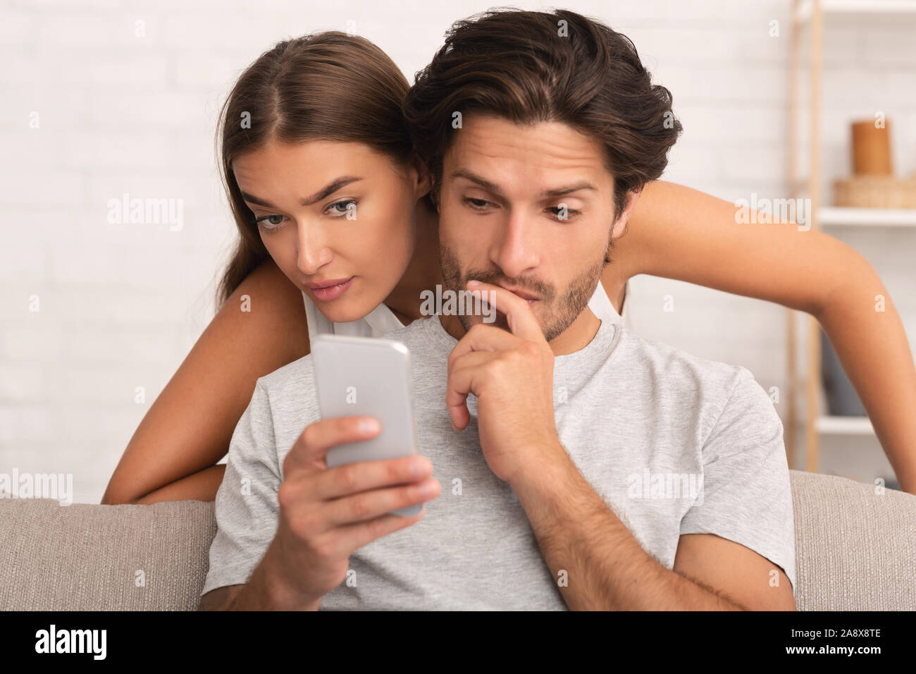Wife Spying On Husband While He Chatting On Phone Indoor Stock Photo