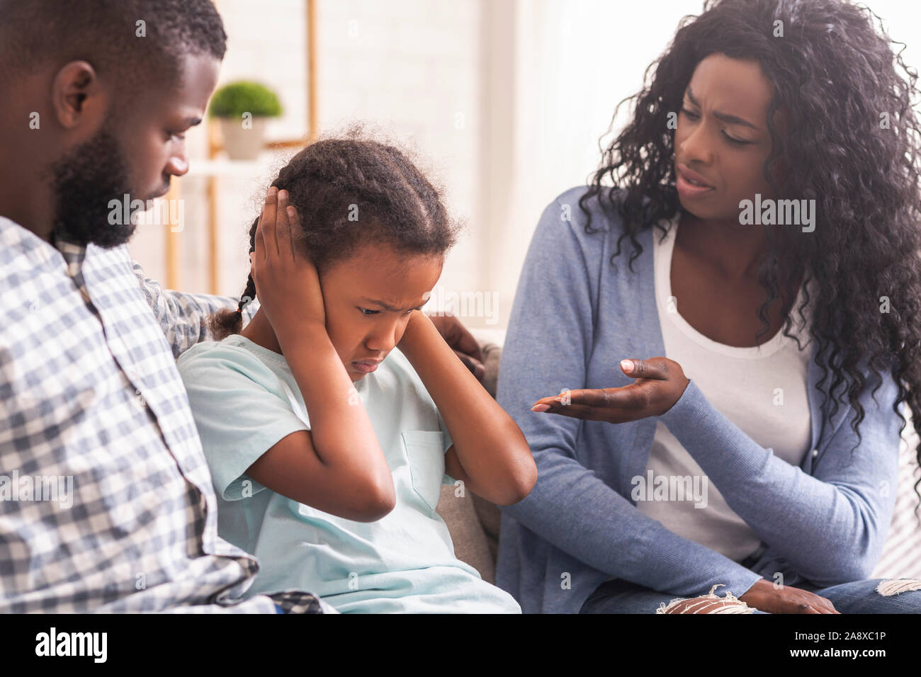 Little girl closing her ears not to listen parents scolding Stock Photo