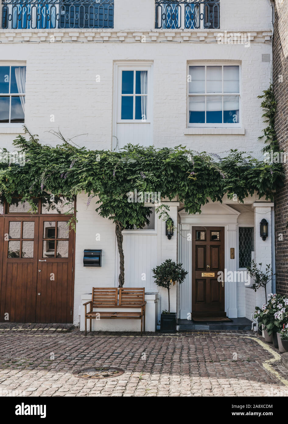 Facade of a typical mews house with a climber plant and wooden bench