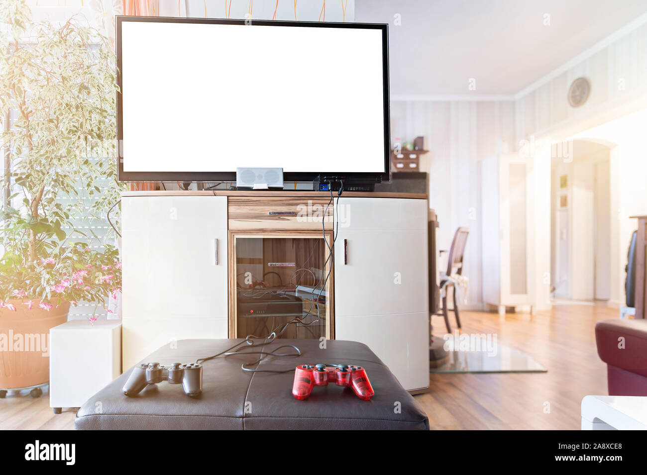 A widescreen TV with Copy Space. In the foreground are joysticks and a game console. Authentic home interior. Stock Photo