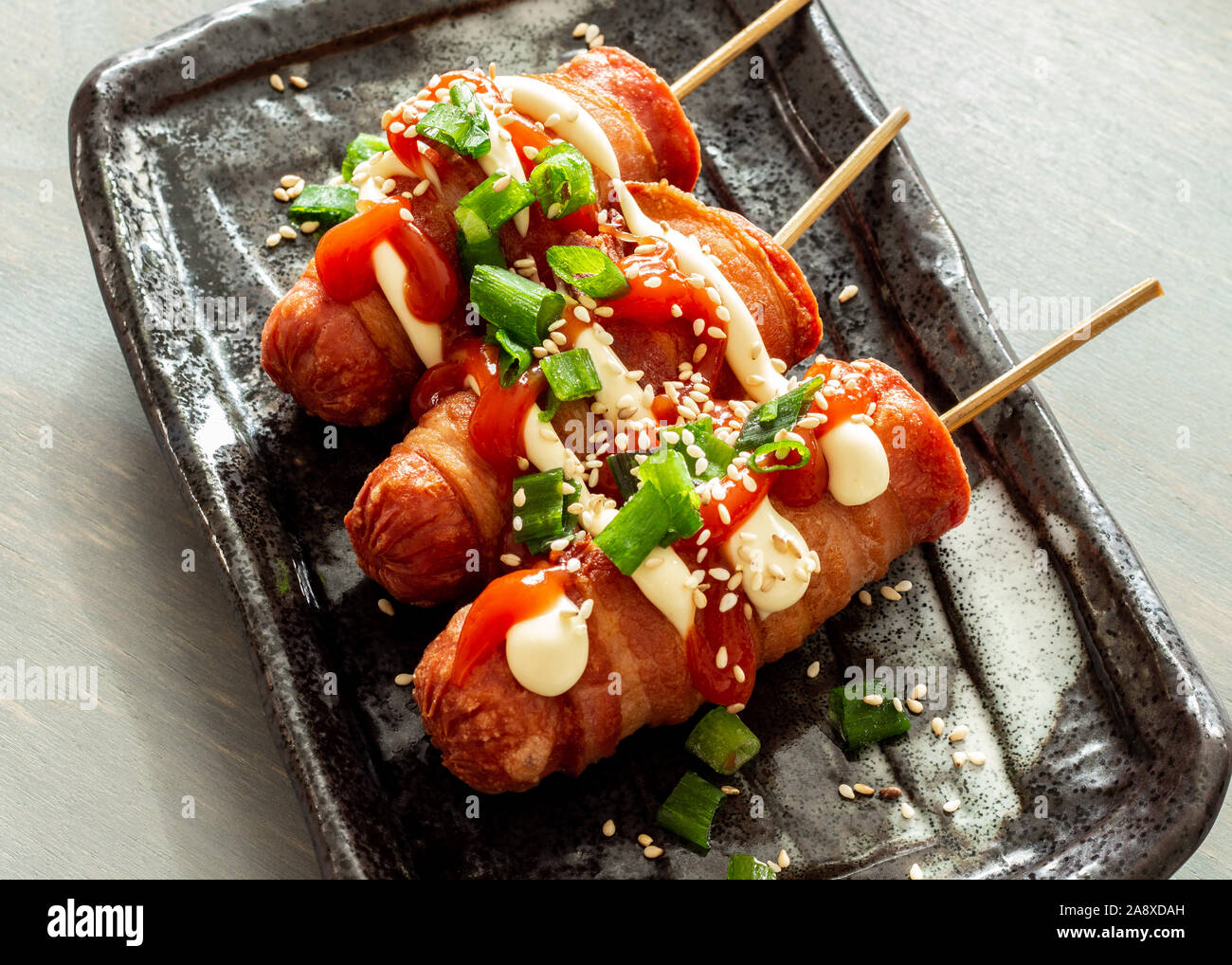 Bacon wrapped hot dogs on a stick. Topped with mayo, ketchup, spring