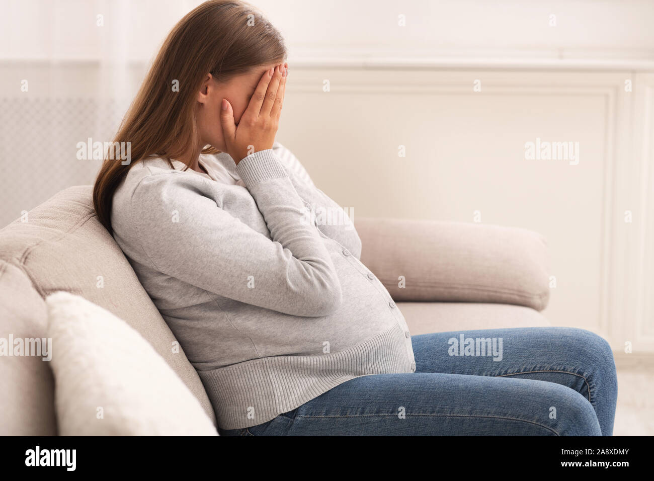 Pregnant Lady Crying Covering Face With Hands Sitting At Home Stock Photo