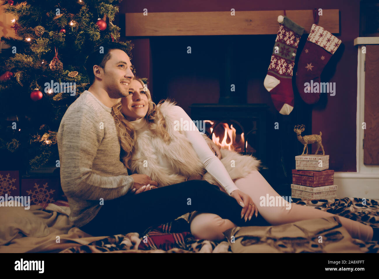 Loving couple by a roaring log fire at Christmas Stock Photo