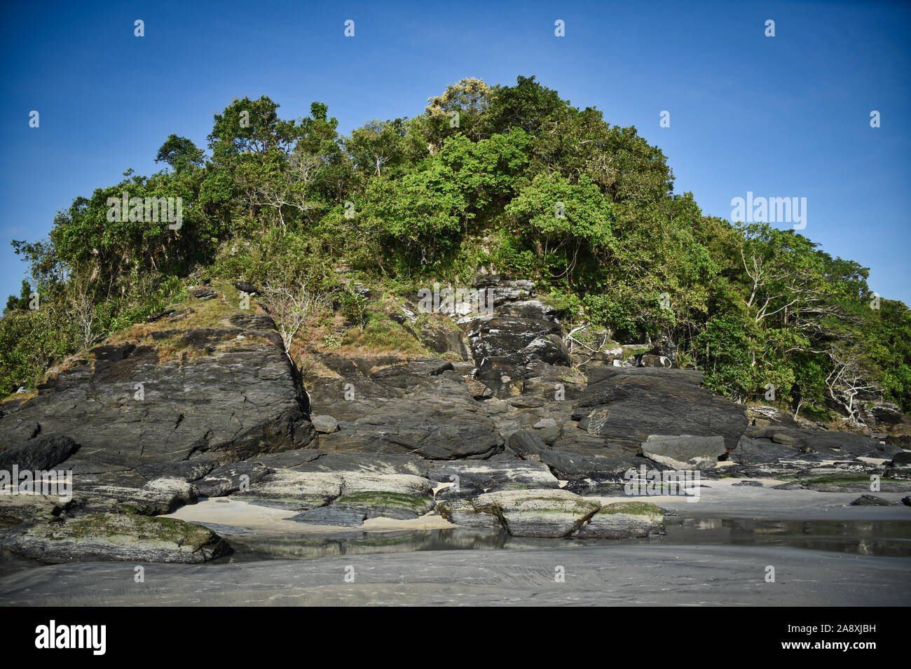 Hillside with black rocks and green trees, plants on the shores of the sandy beautiful exotic and stunning Cenang beach in Langkawi island, in Malaysi Stock Photo