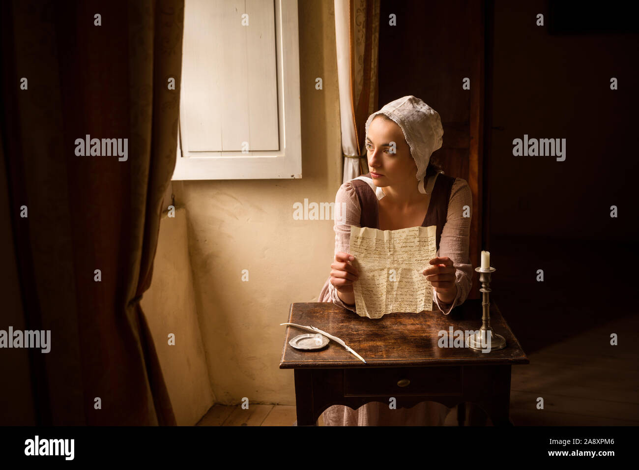 Vermeer style portrait of a young maid in renaissance costume reading a letter at her window Stock Photo