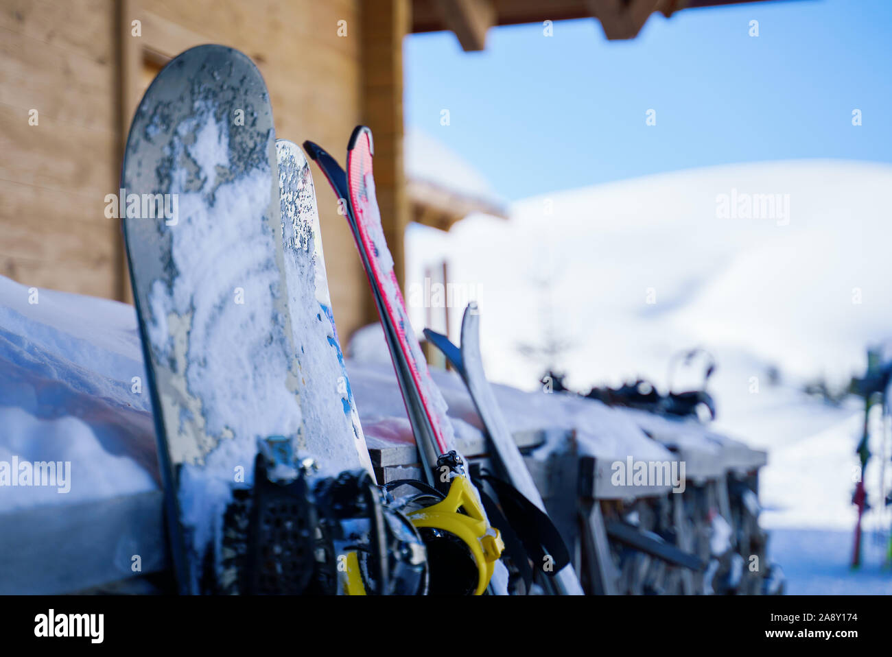 Image of multi-colored skis and snowboards in snow at winter resort in afternoon. Blurred background. Stock Photo