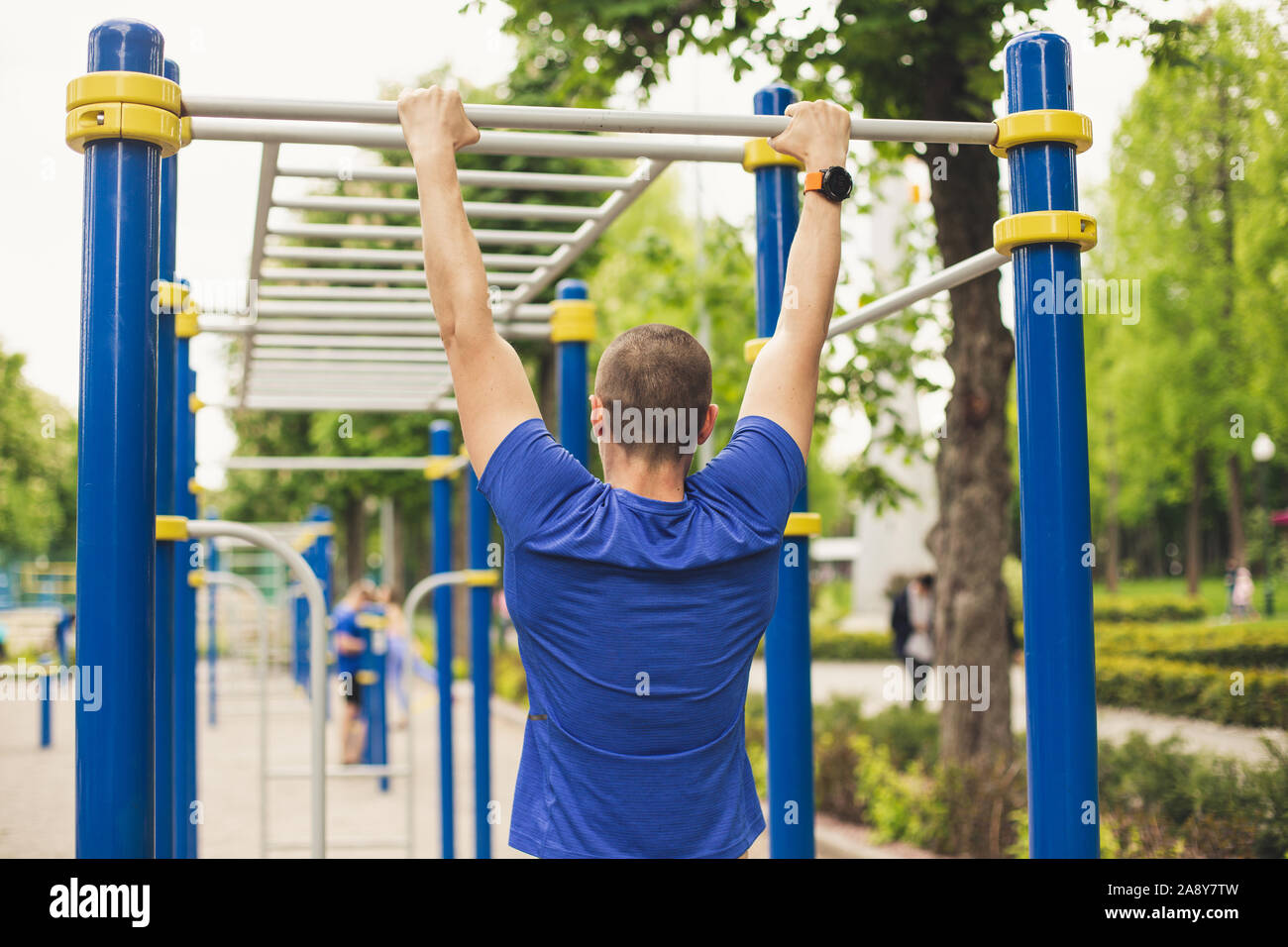 Man doing pull ups workout in the ground park. View from back