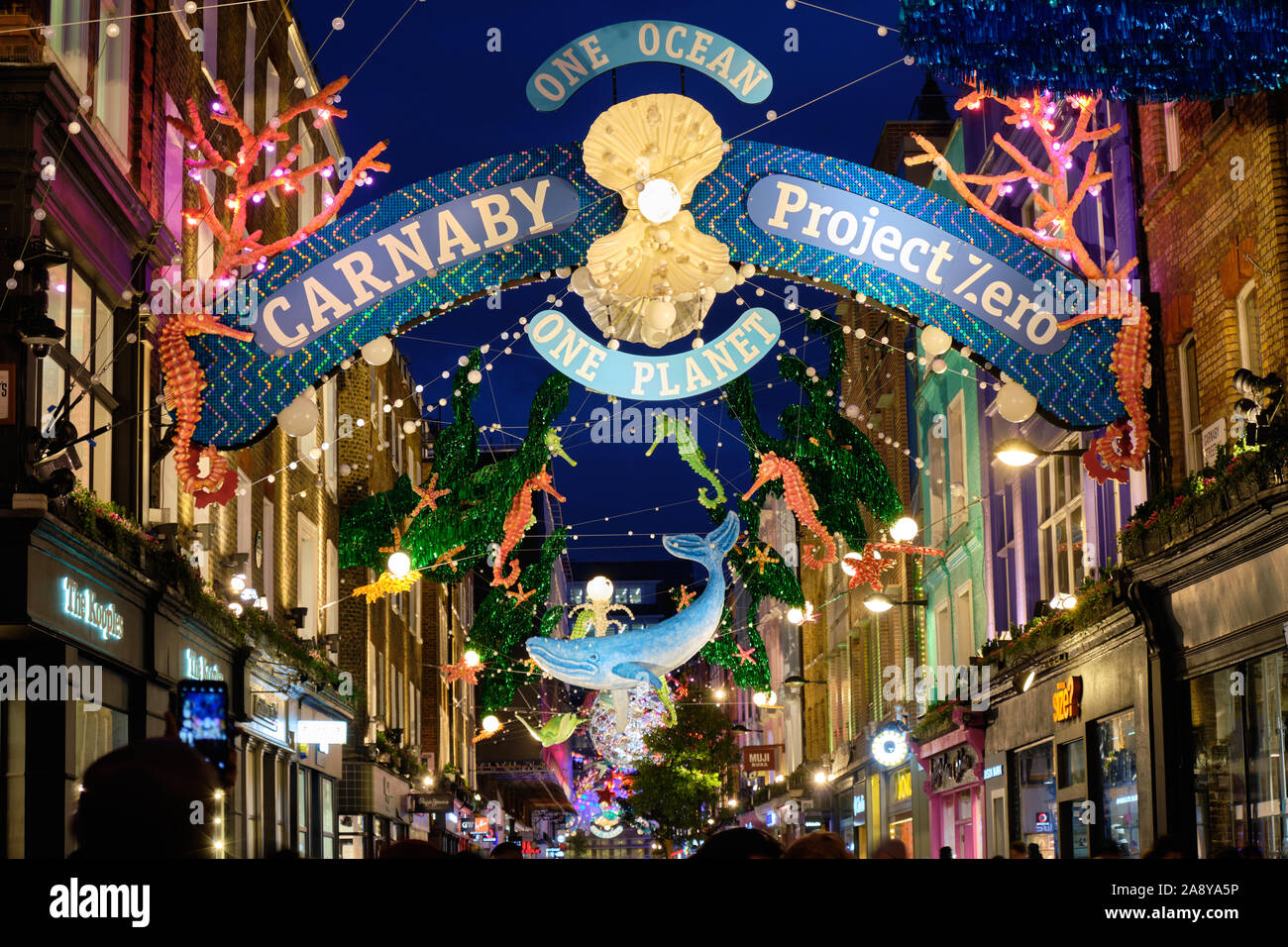 2019 Carnaby Street theme: One Ocean Sealife Christmas lights decoration made from recycled material. Colourful display lit up in evening, with crowd Stock Photo