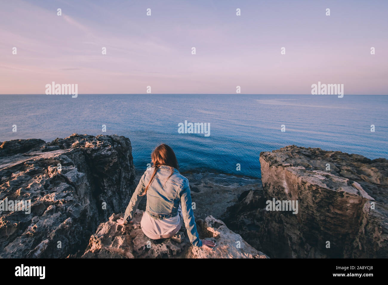 Woman traveler sitting near sea on top of cliff in summer mountains and enjoying view of nature and sea. Cape Greco, Cyprus, Mediterranean Sea. Sunris Stock Photo