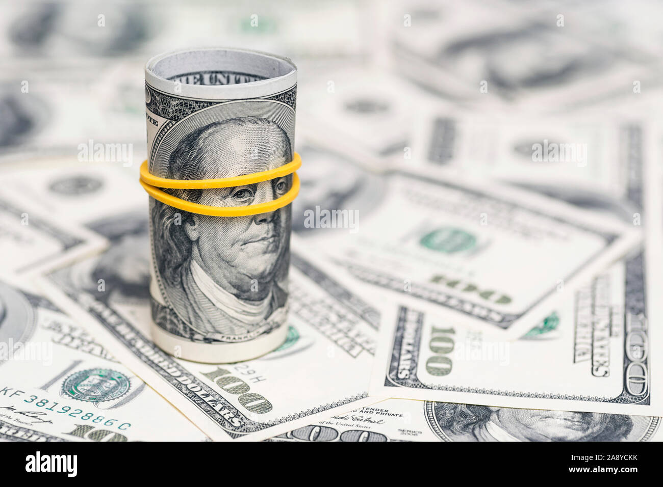 A roll of 100 dollar bills close-up on a pile of American dollars. Background from banknotes of 100 american dollars. Financial concept. Stock Photo