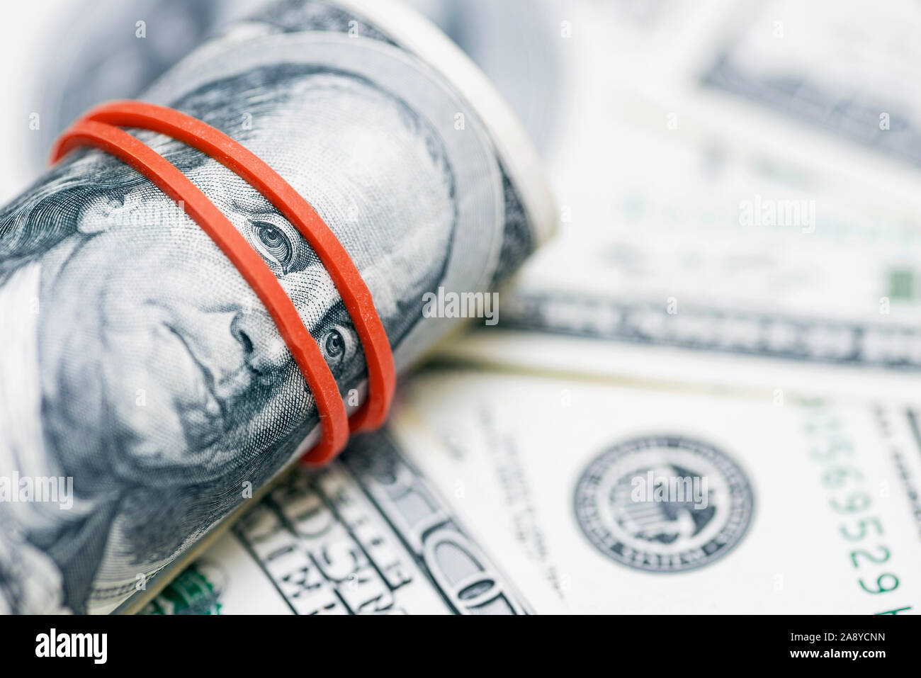 A roll of 100 dollar bills close-up on a pile of American dollars. Background from banknotes of 100 american dollars. Financial concept. Stock Photo