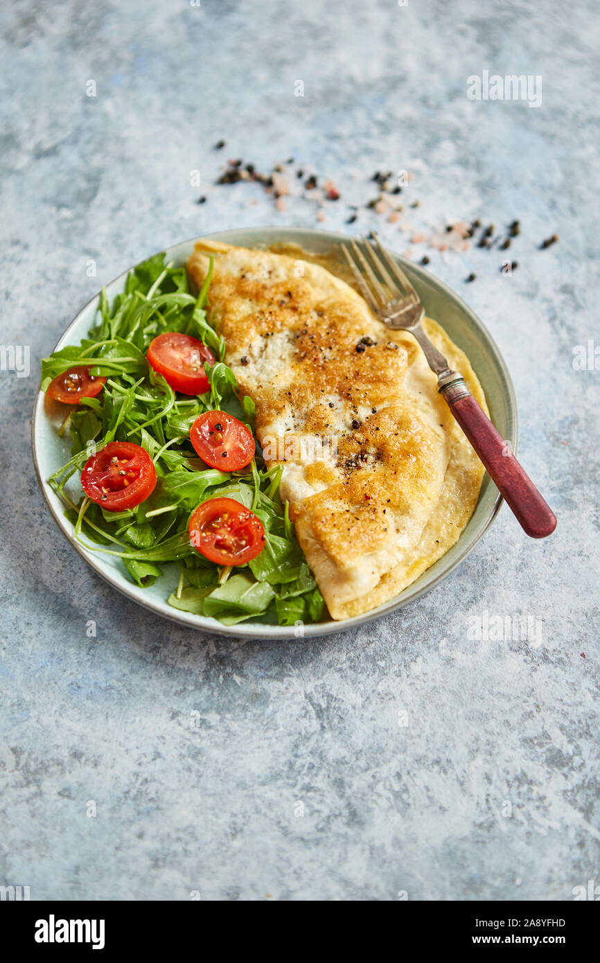 Classic egg omelette served with cherry tomato and arugula salad on side Stock Photo