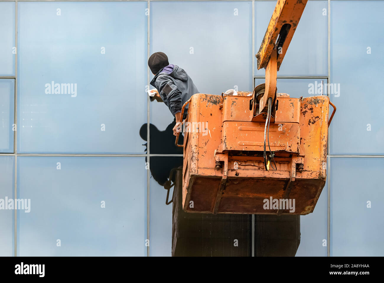 A male unidentifiable worker cleaning the windows of a building standing on a crane, outdoors Stock Photo