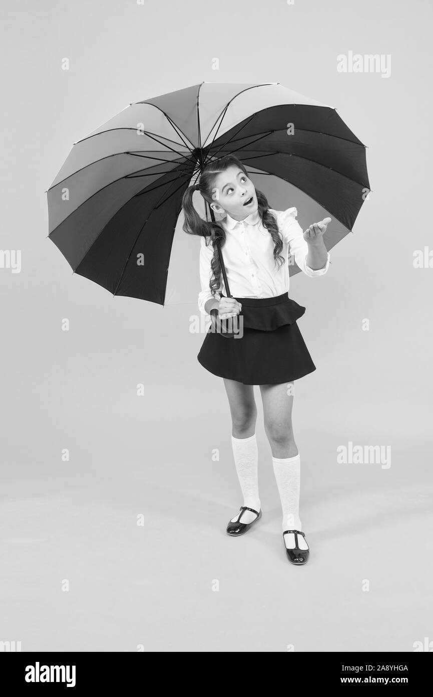 It looks like rain. Cute little girl checking up rain on yellow background. Adorable small schoolchild holding rain bow colored umbrella. Rain forecast. Stock Photo
