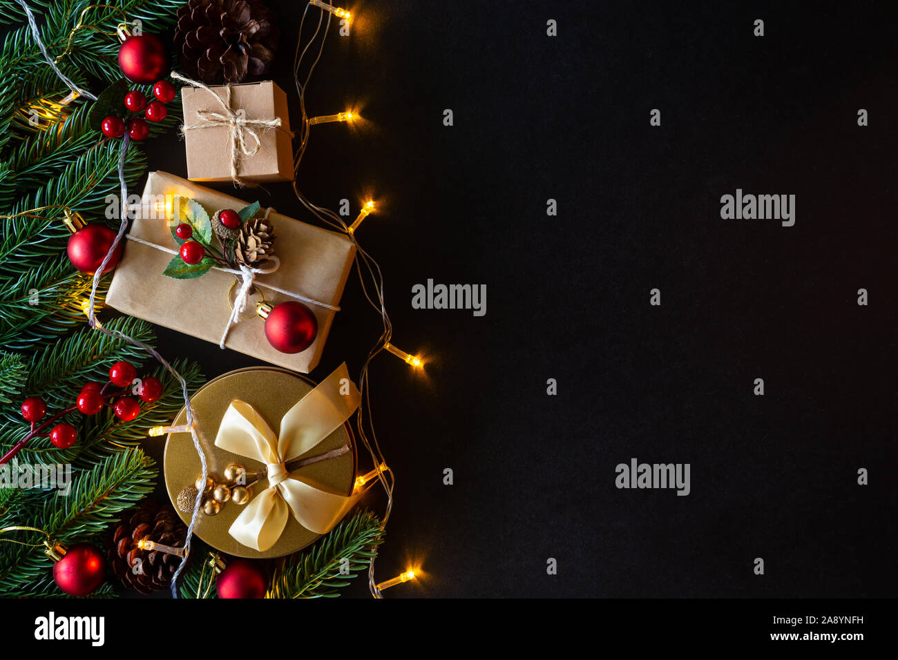 Holiday Christmas card background with festive decoration ball, stars, snowflakes, gift box, pine cones on a black background from Flat lay, top view. Stock Photo