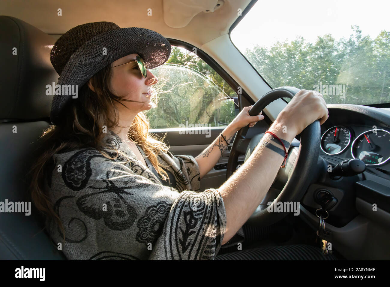 Young woman driving her big SUV. General view of cabin from the sideways. Woods and green environment at backgorund. Lifestyle. Stock Photo