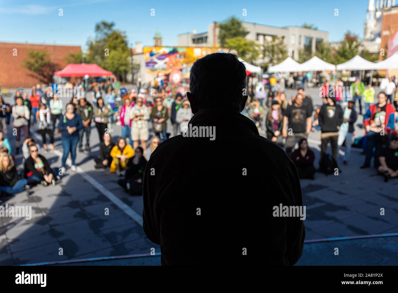 Silhouette of man on a stage talking to a crowd in a public space. People standing and sitting listening to his discourse during climate change protest Stock Photo