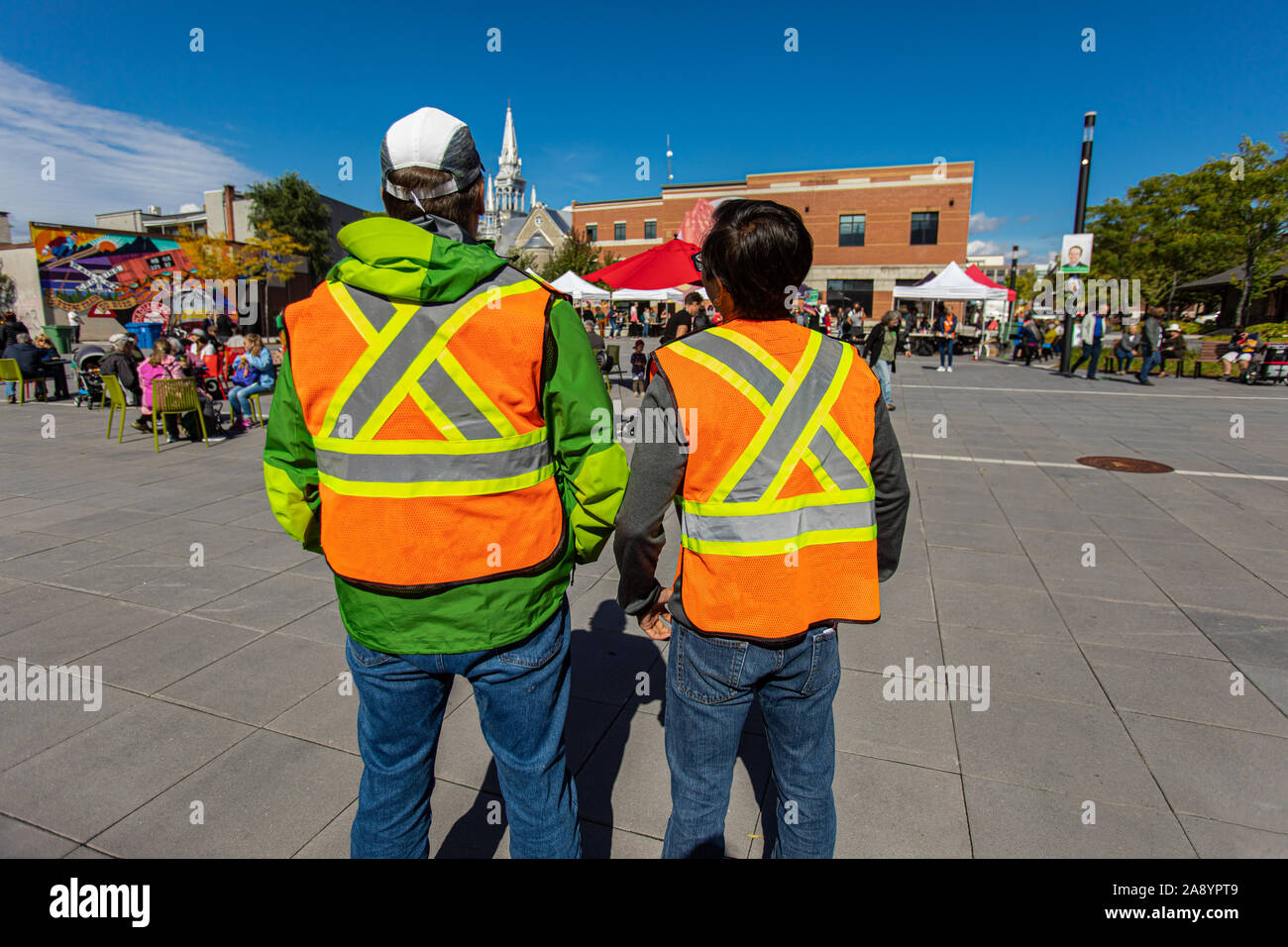Two men from the back with high emergency clothing at public space protecting and looking out at climate change protest.  Stock Photo