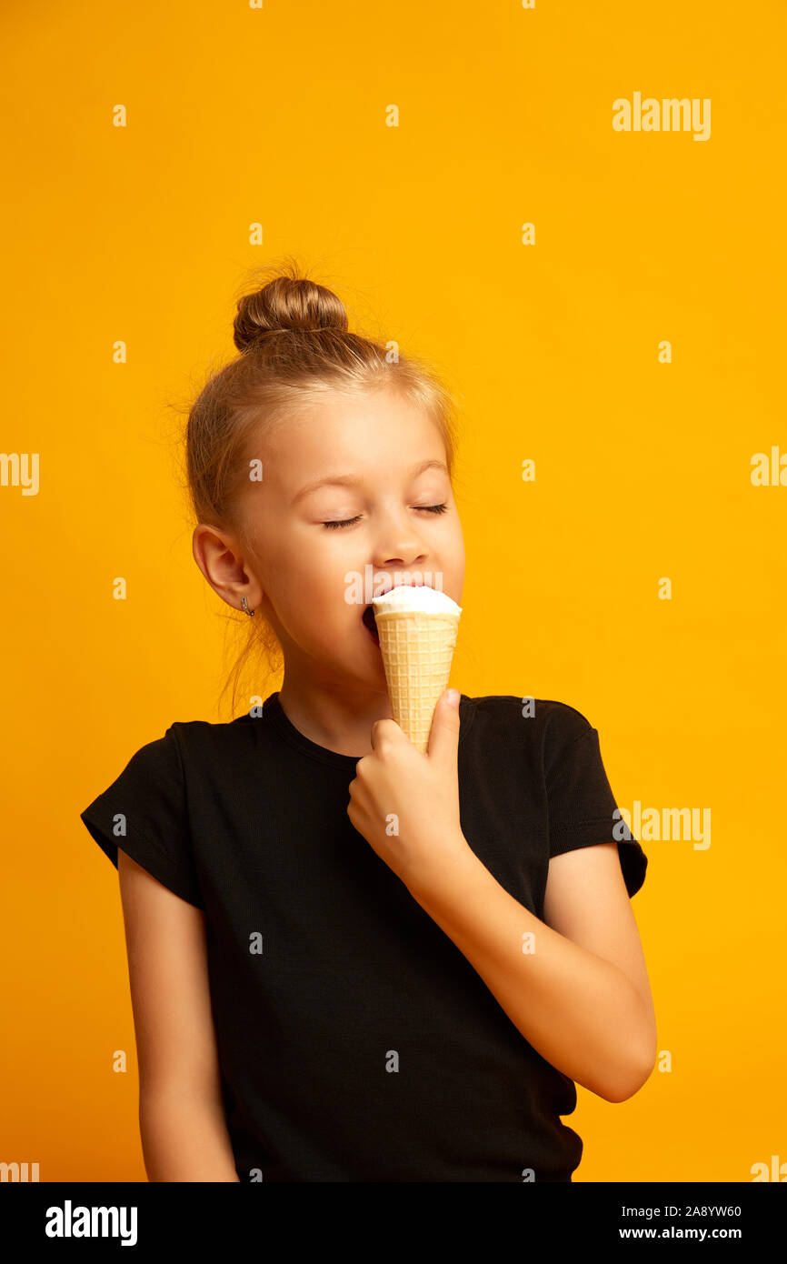 Little dancer in a swimsuit with closed eyes eats ice cream in a studio on a yellow background Stock Photo