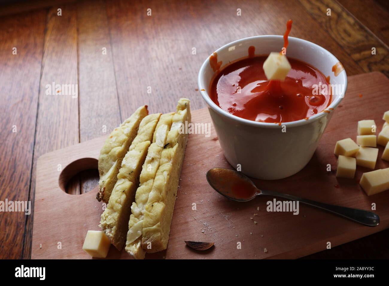 cheese cube falling into tomato soup in a white bowl and making a messy splash with more cheese
