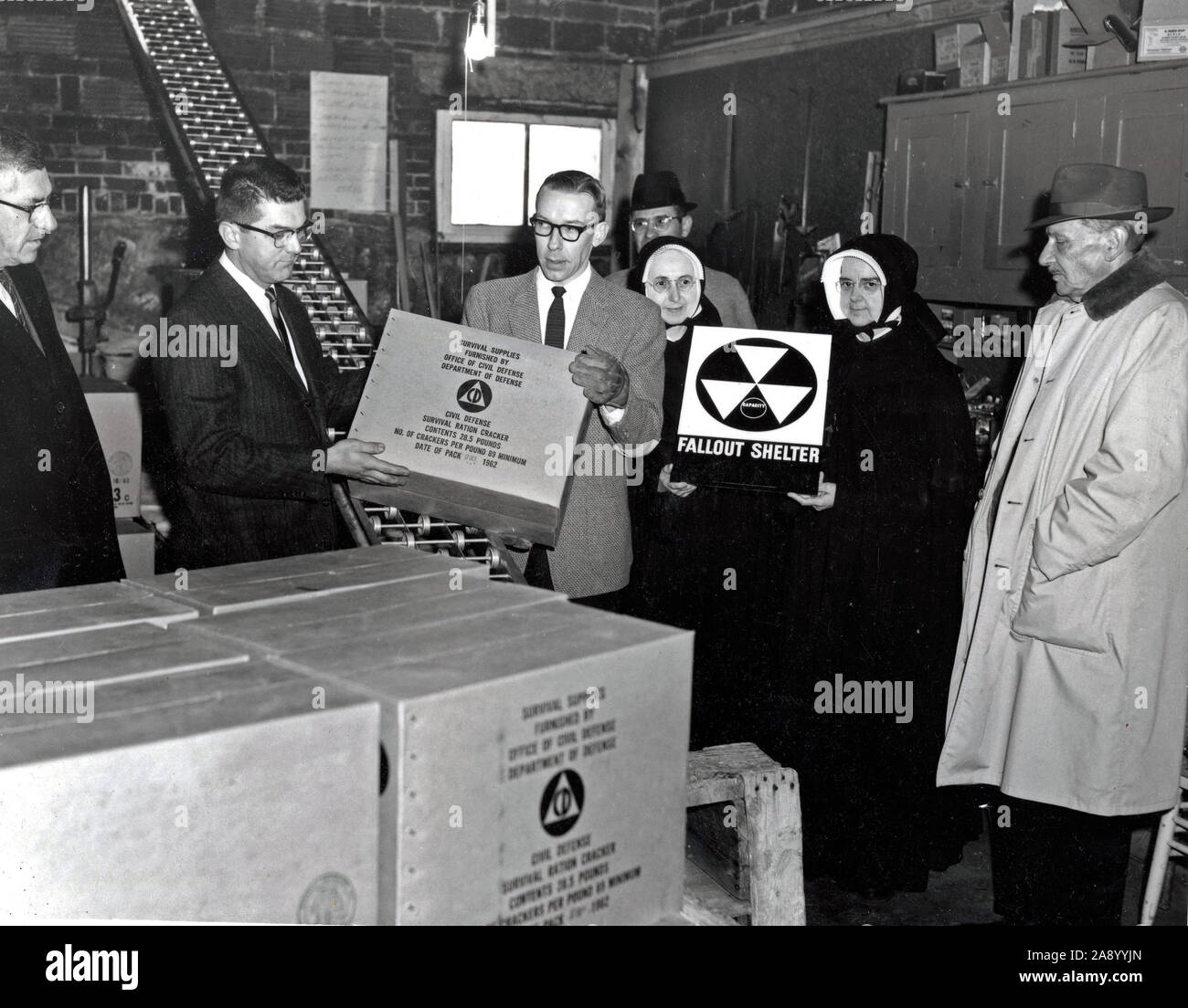 This photograph depicts a fallout shelter being furnished with Civil Defense survival rations at Villa Augustina Academy in Goffstown, New Hampshire. Mother Wilfred and Mother Superior Liguori of the Religious of Jesus and Mary, the religious order that founded and operated the school, appear in the photograph, holding a fallout shelter sign. Stock Photo