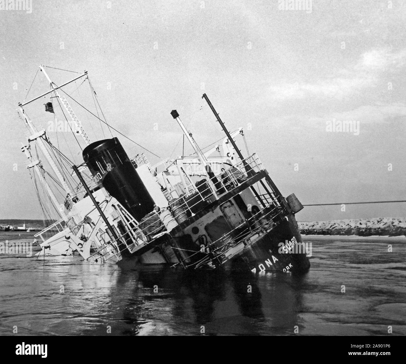 This photograph depicts the cargo ship Arizona Sword listing to port as it sinks in the Cape Cod Canal. On May 5, 1951, the vessel was involved in a collision with the SS Berwindvale near the east end of the canal in Sandwich, Massachusetts. Her cargo of 48,000 tons of sulphur would be successfully salvaged by midsummer. Stock Photo