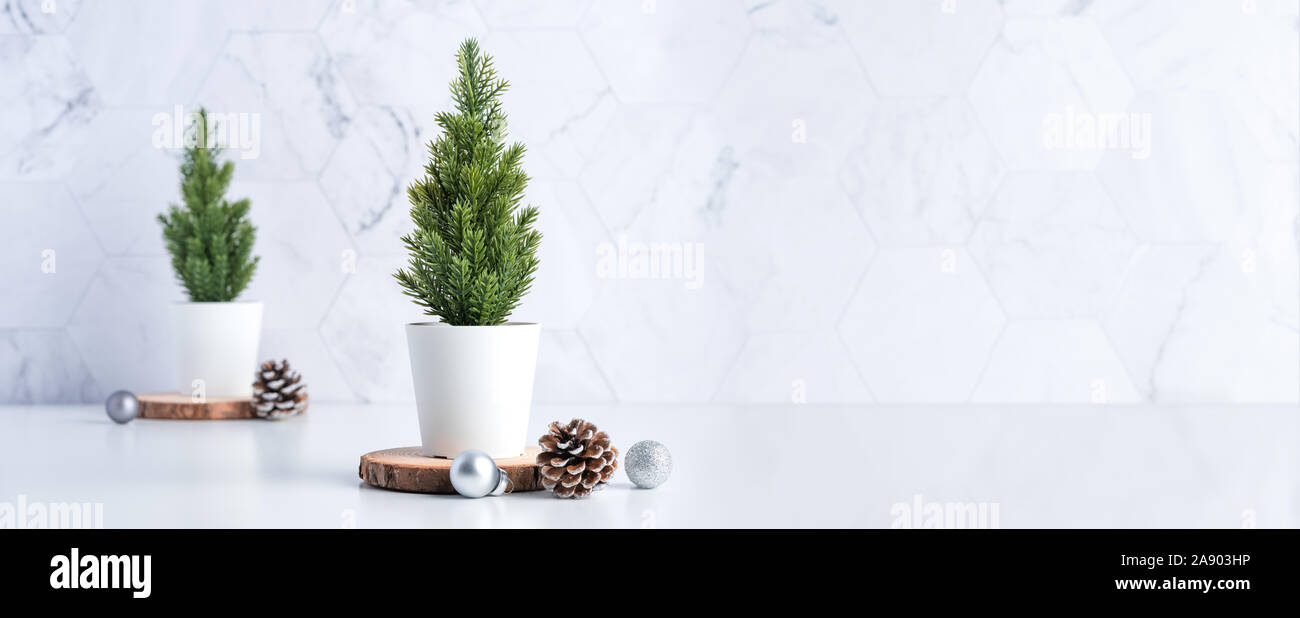 christmas tree with pine cone,decor xmas ball on wood log at white table and marble tile wall background.clean minimal simple style.holiday still life Stock Photo