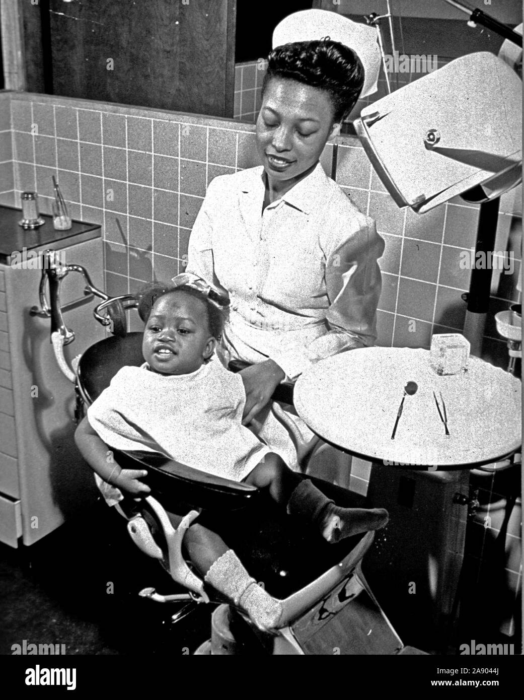 African American little girl is sitting in a dental chair with a dental assistant standing next to her. Stock Photo