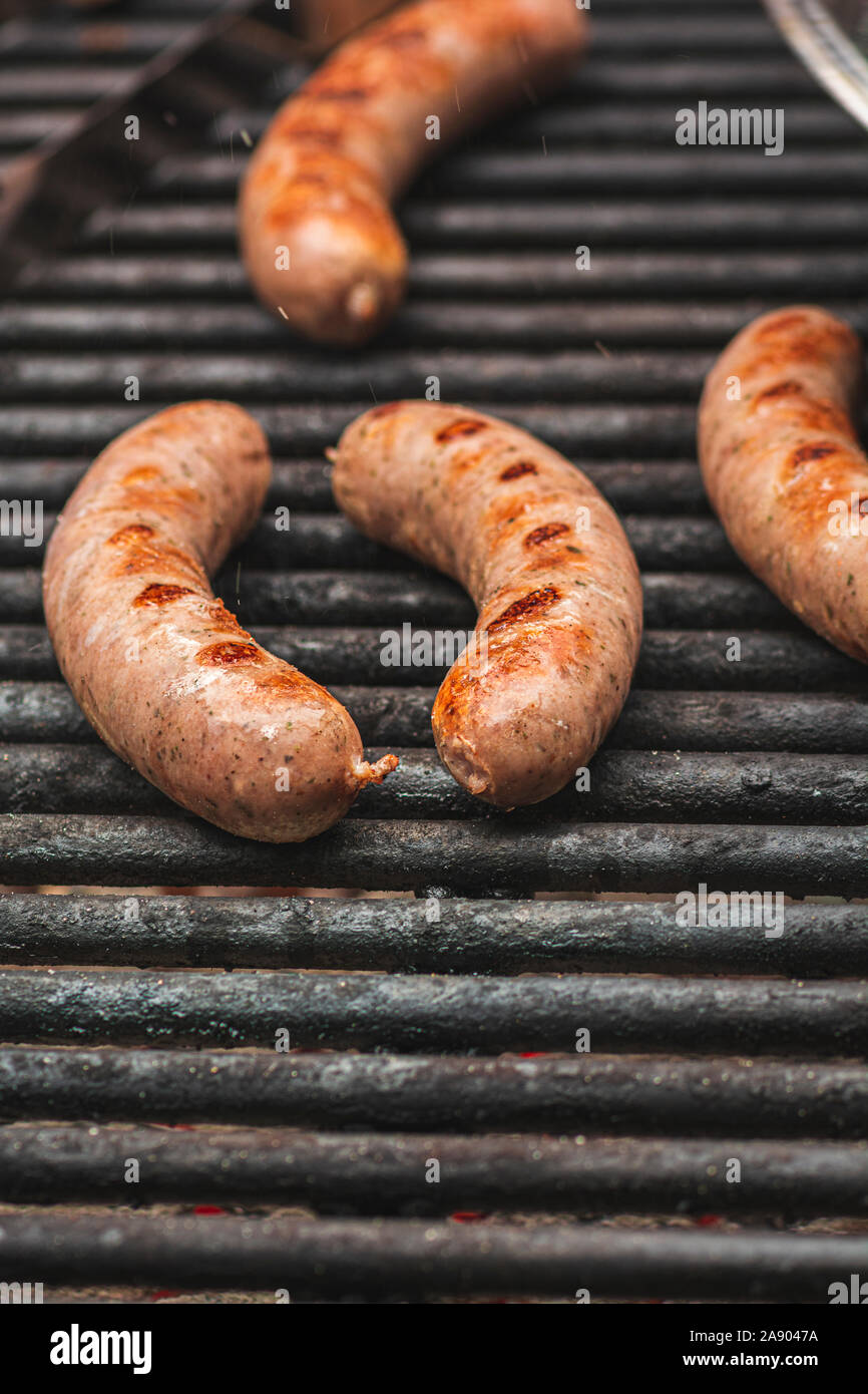 Sizzling juices jumping off savory brats cooking on an outdoor iron grill. Stock Photo