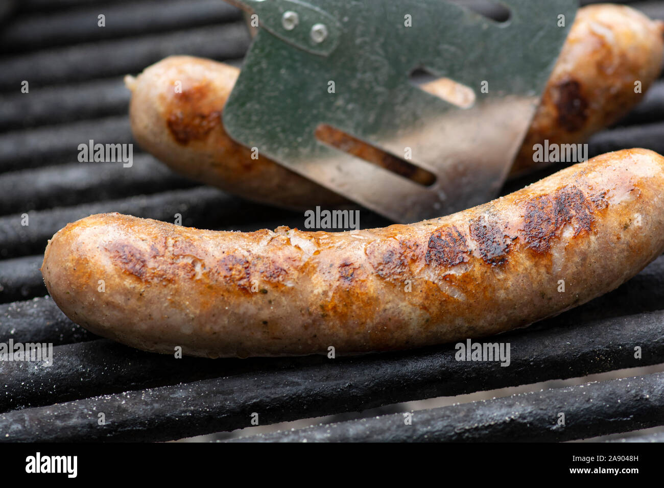 Savory brats cooking on an outdoor iron grill. Stock Photo