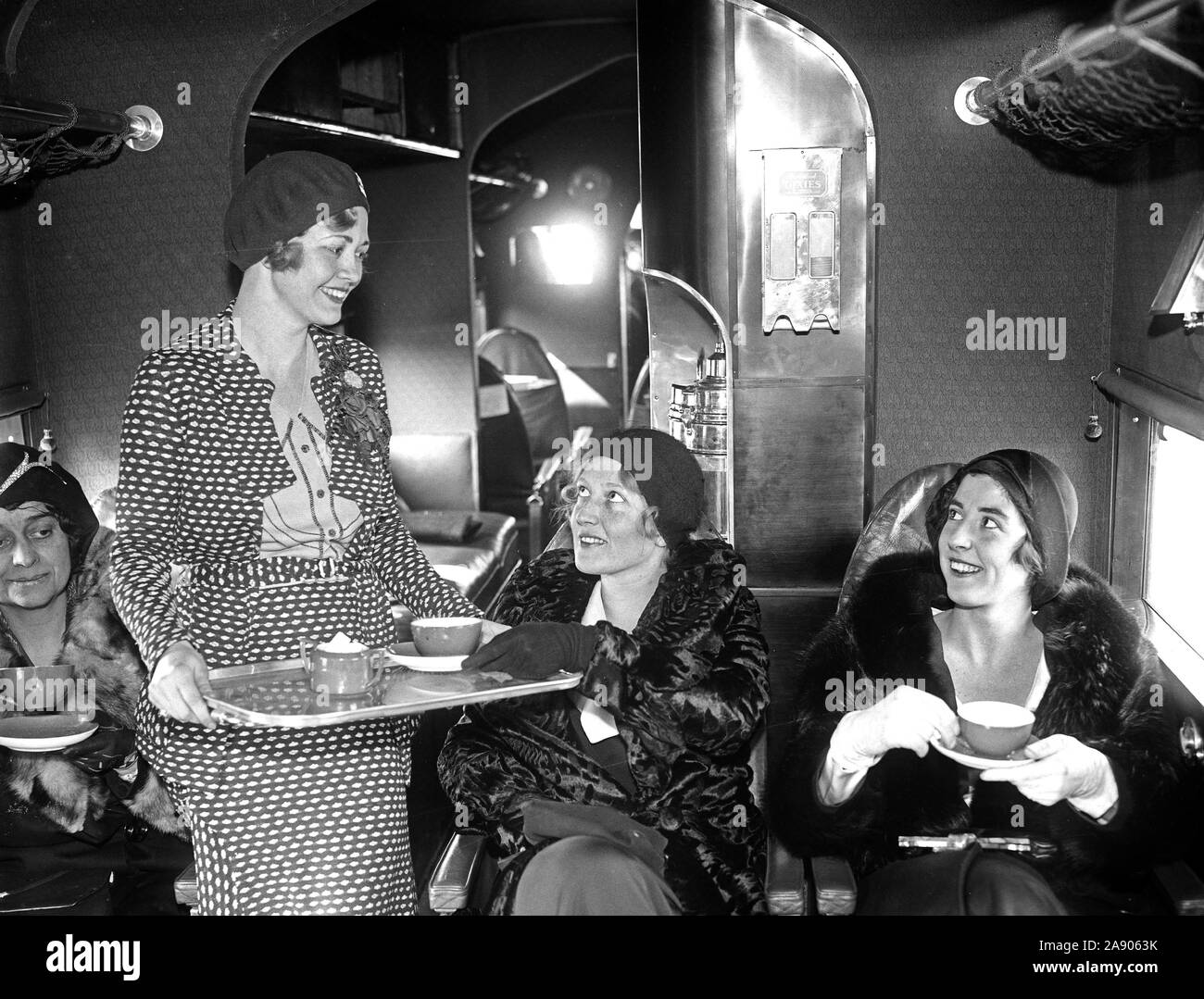 Miss Wanda Wood, hostess for the Eastern Air Transport, serves tea for two, Misses Charlotte Childress and Elizabeth Hume, aboard one of the line's passenger planes ca. 1930 Stock Photo