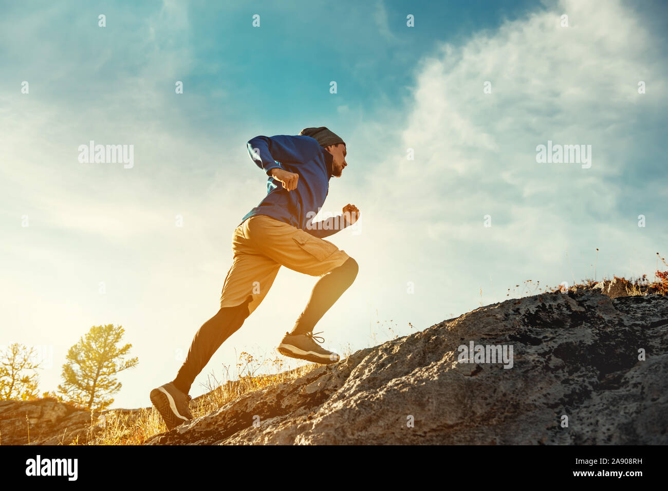 Skyrunner athlete runs uphill against sunset or sunrise sky and sun. Skyrunning concept Stock Photo