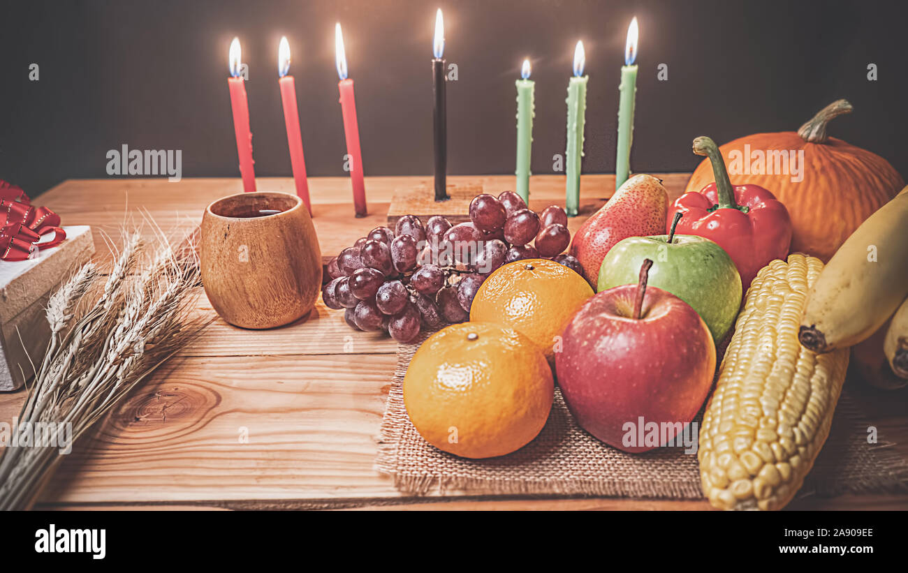 Kwanzaa holiday concept with decorate seven candles red, black and green, gift box, pumpkin,corn and fruit on wooden desk and background. Stock Photo