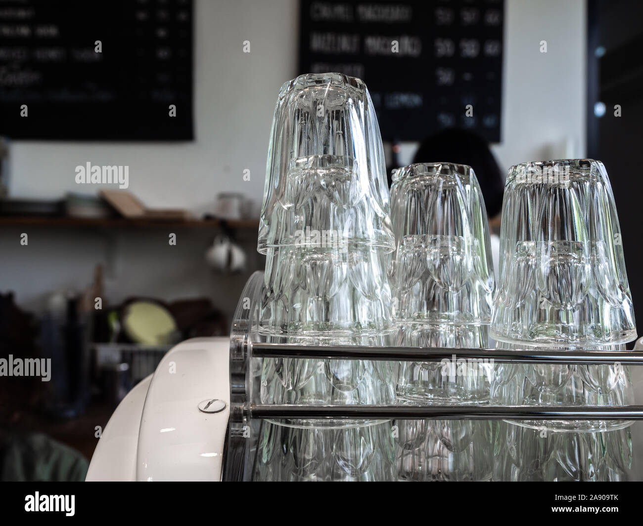 Stacks of clean empty glasses on stainless steel shelf in cafe. Piles of upside down drinking water glasses. Stock Photo
