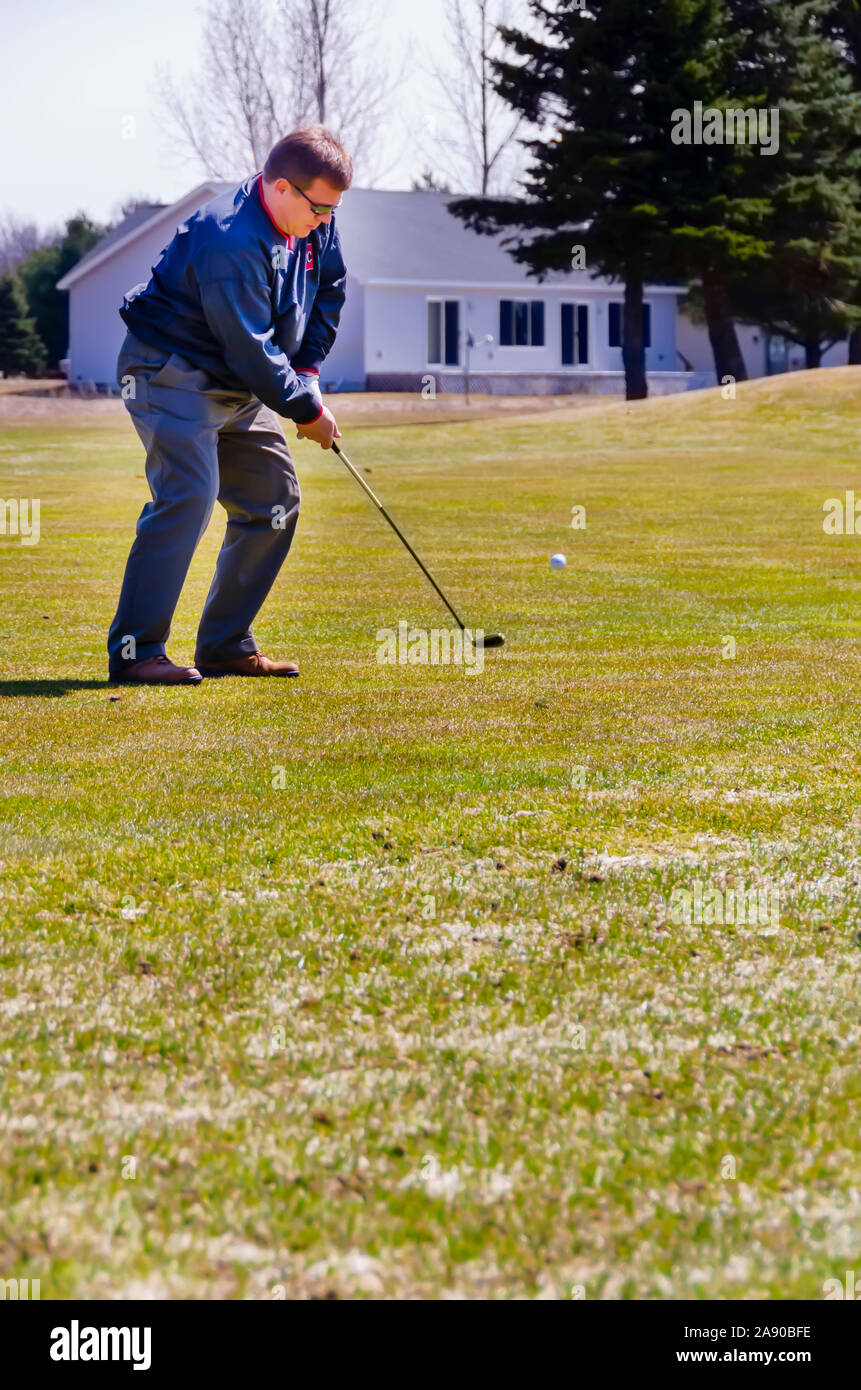 A golfer hitting the ball from the fairway with an iron. Stock Photo