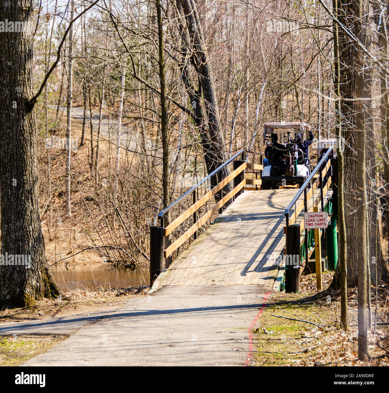 Golfers on golf carts crossing a wooden bridge on a golf course while on their way to the next hole. Stock Photo
