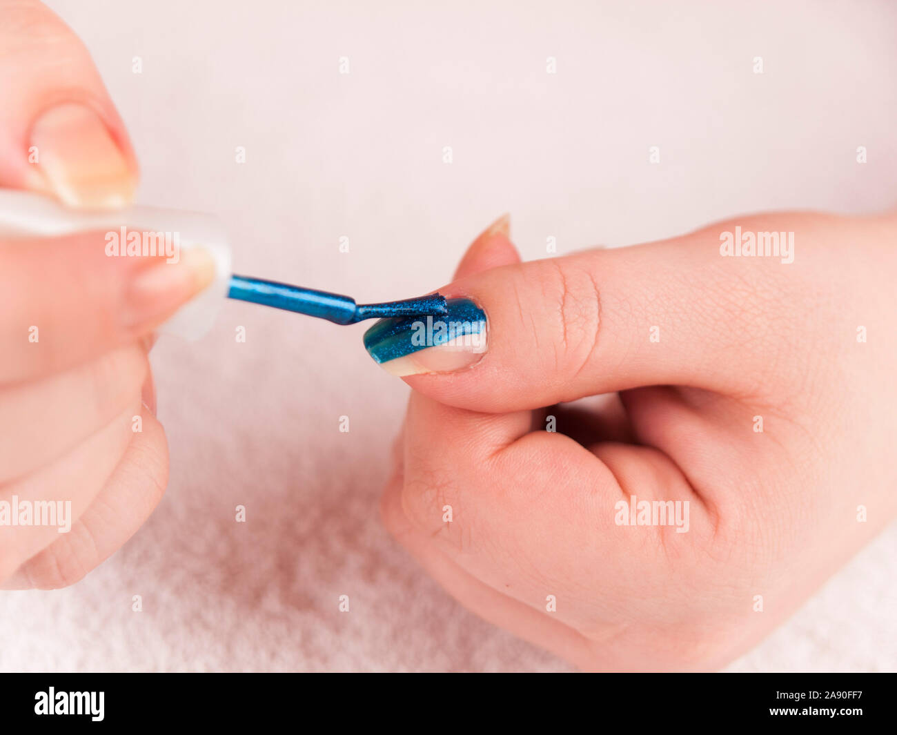 Detail of applying dark blue nail polis on the thumb Stock Photo