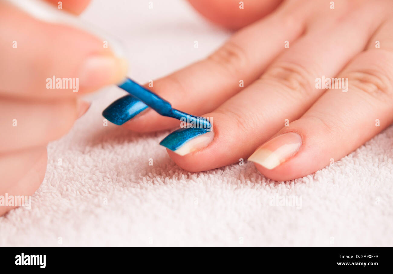 Woman applying dark blue shiny nail polish on middle finger Stock Photo