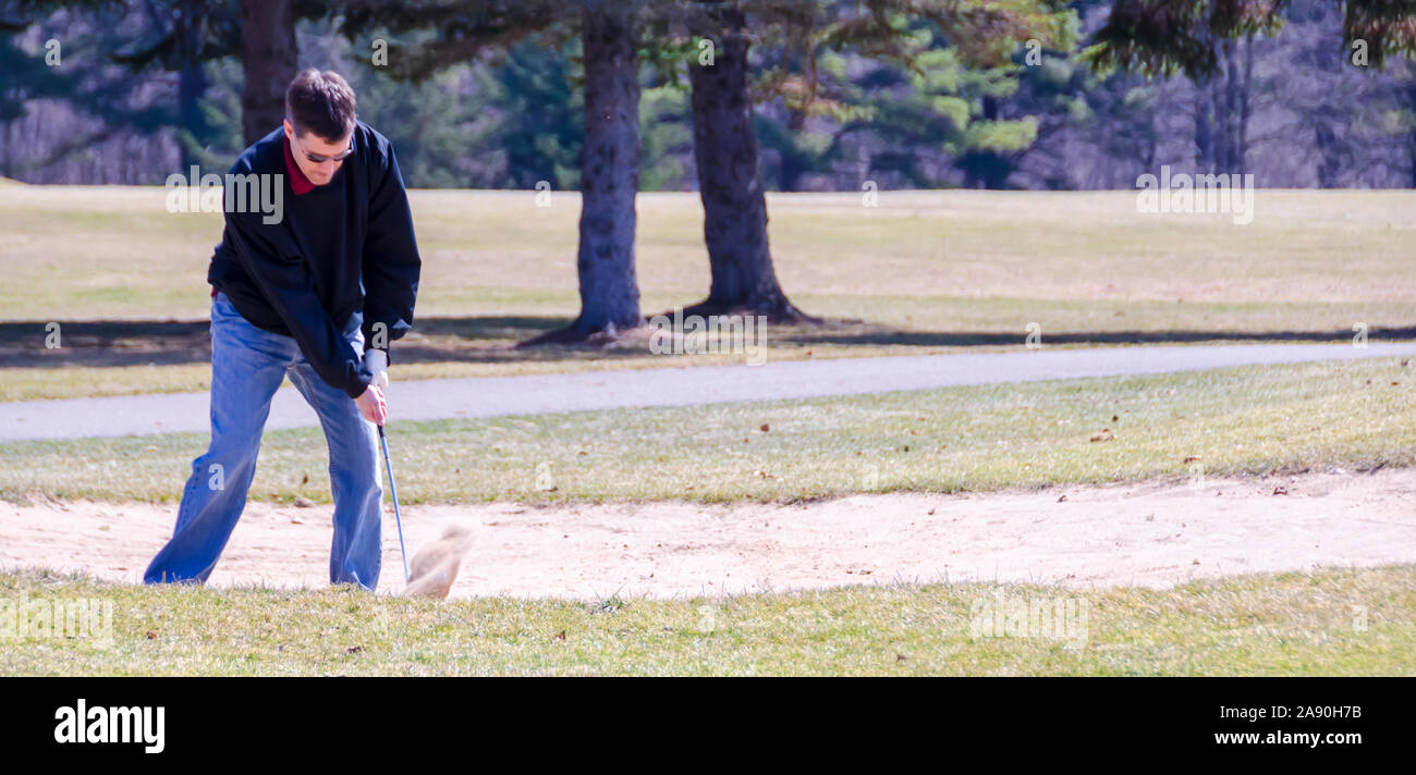 A golfer hitting a golf ball in the bunker with a sand wedge. Stock Photo