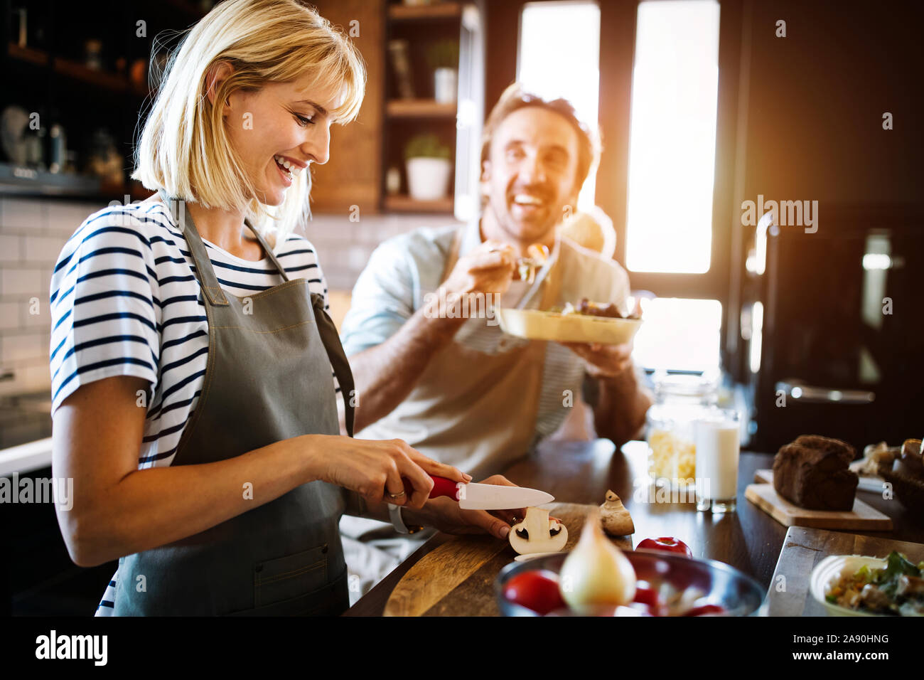 Beautiful young couple is smiling while cooking together in kitchen at ...