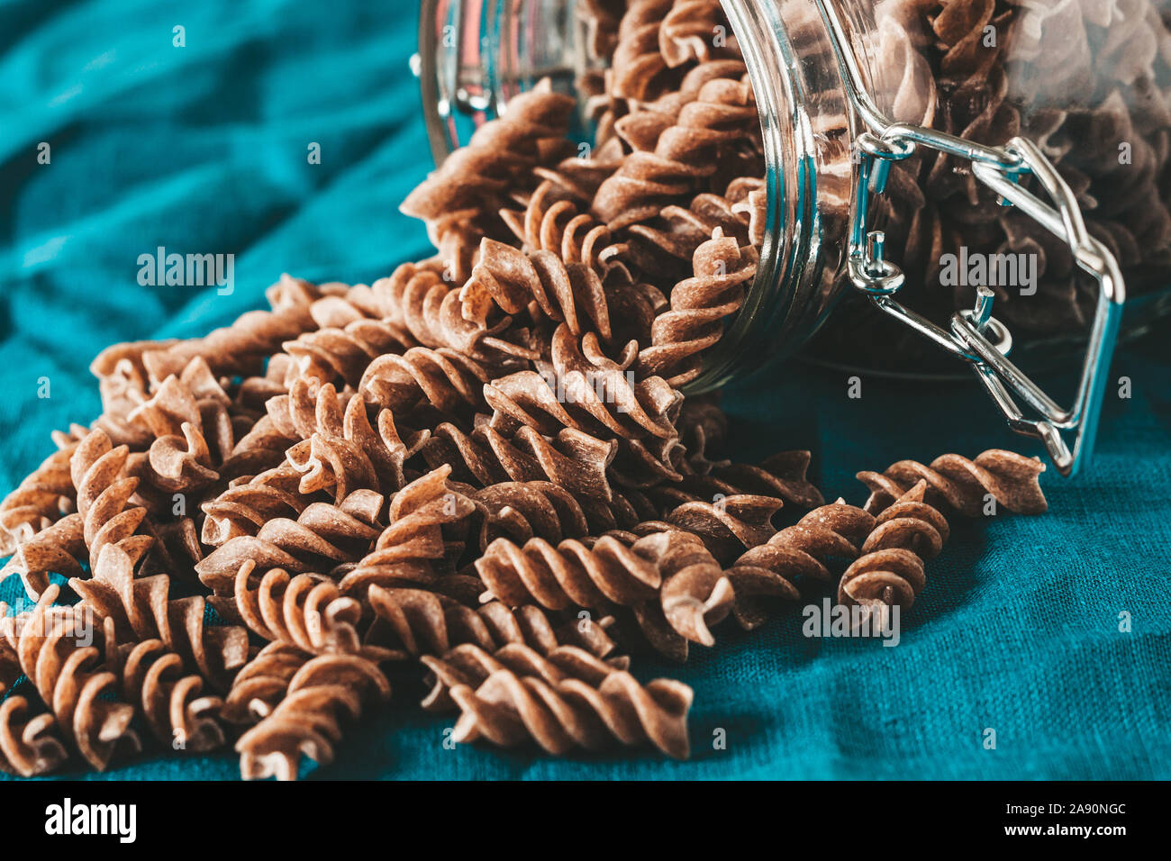 Dark brown whole grains of pasta in a glass jar in the kitchen on a blue linen cloth Stock Photo