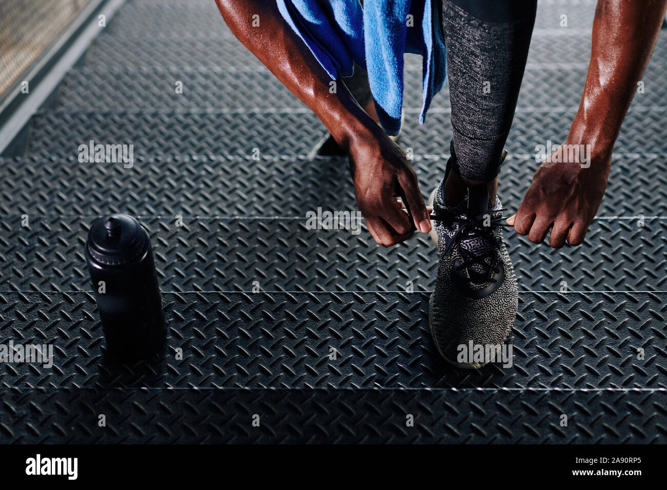 Close-up image of sweaty sportsman standing on steps and tying shoe laces when resting between sets Stock Photo