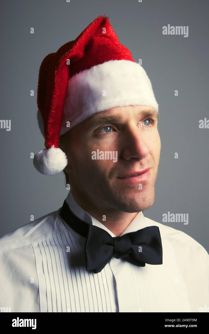 Portrait of young man in formal black tie tuxedo and Santa hat looking up with a thoughtful expression Stock Photo