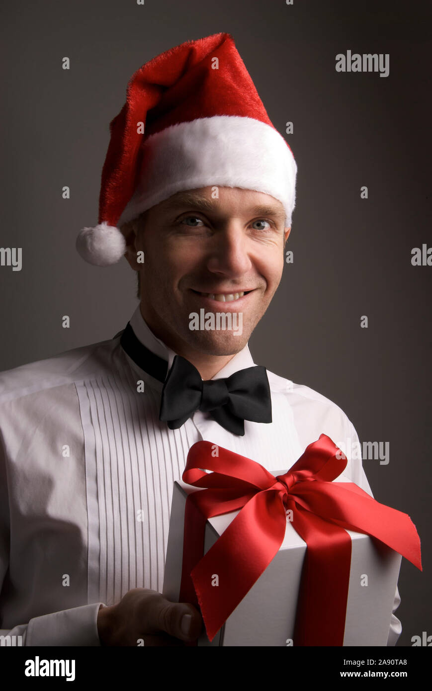 Portrait of young man in formal black tie tuxedo and Santa hat holding