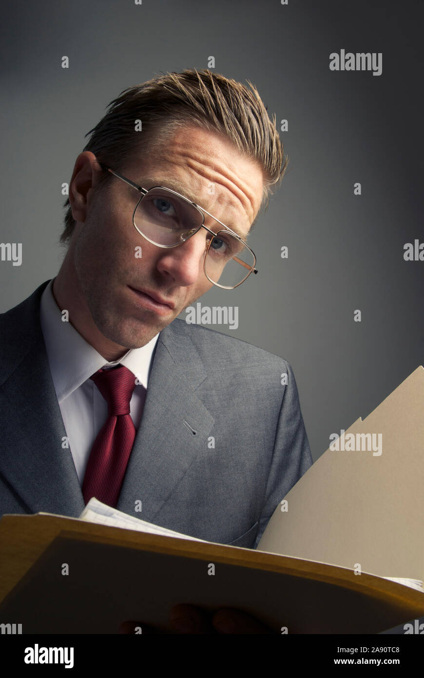 Skeptical businessman holding a file folder looking at the camera with a serious expression Stock Photo