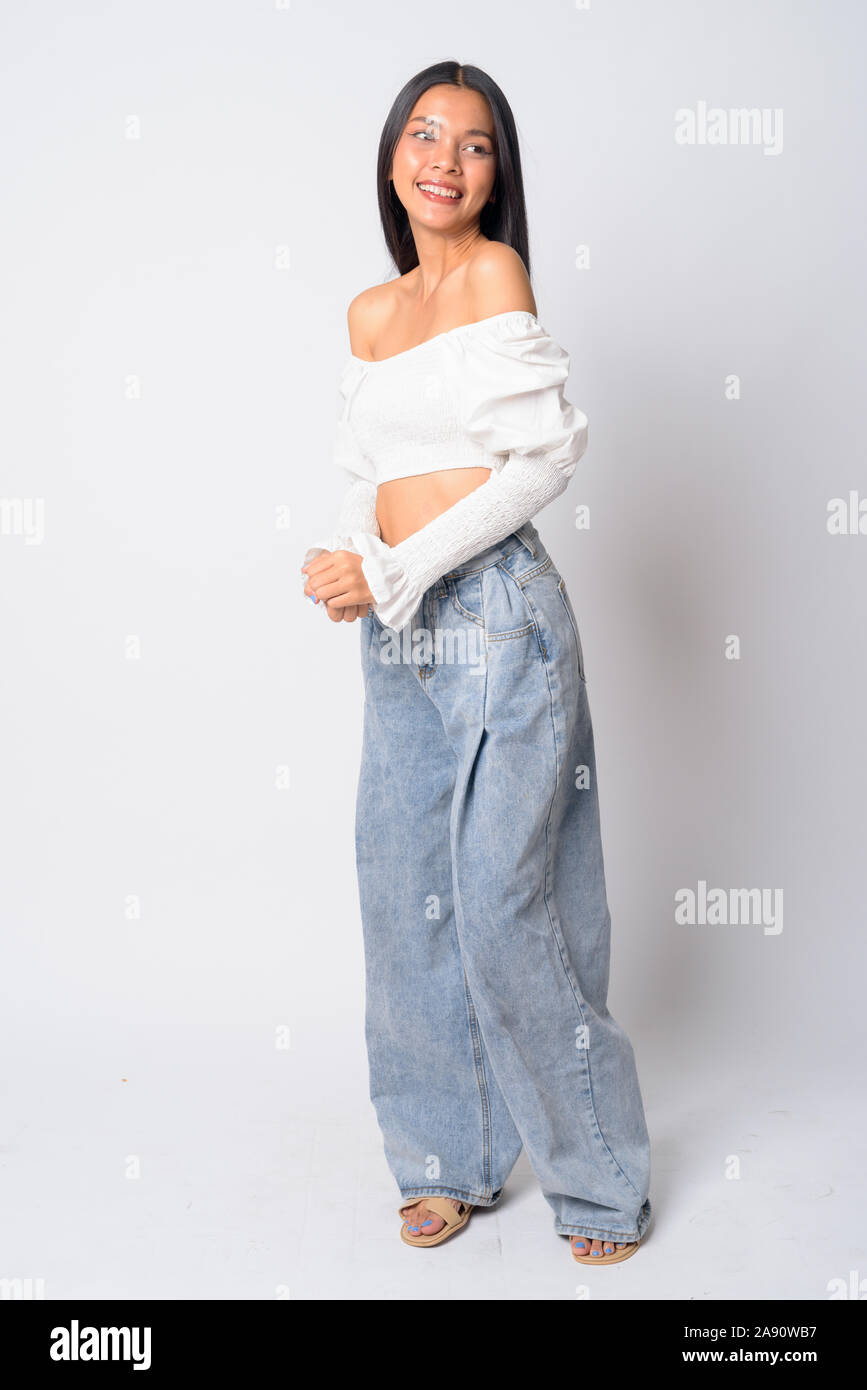 Full body shot of happy young beautiful Asian woman looking over shoulder Stock Photo