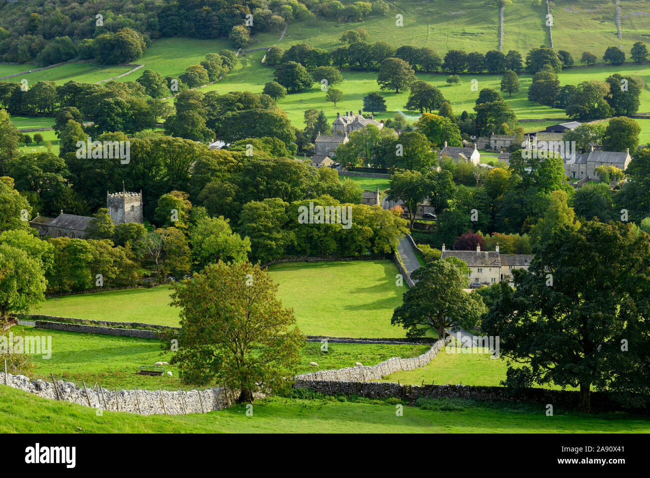 Summer evening sunlight on picturesque Dales village (church & houses) nestling in valley under upland hills - Arncliffe, North Yorkshire, England, UK Stock Photo