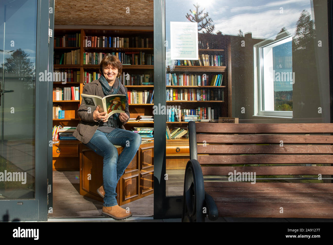 06 November 2019, Saxony, Reinhardtsdorf: Evelin Arnold sits on a stool in  the book stop in Reinhardtsdorf near Bad Schandau in Saxon Switzerland. The  former bus shelter was converted into a book